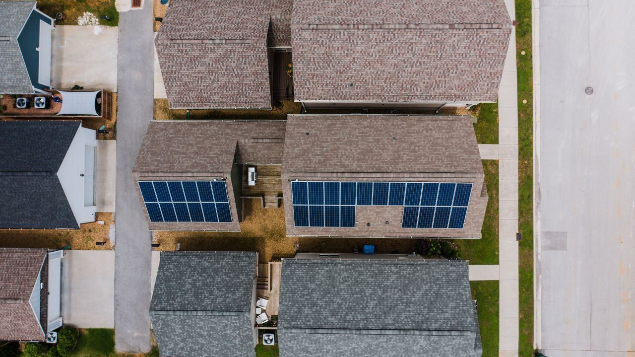 gallery-01 Top-down view of suburban houses featuring solar panels on roofs, showcasing renewable energy use.