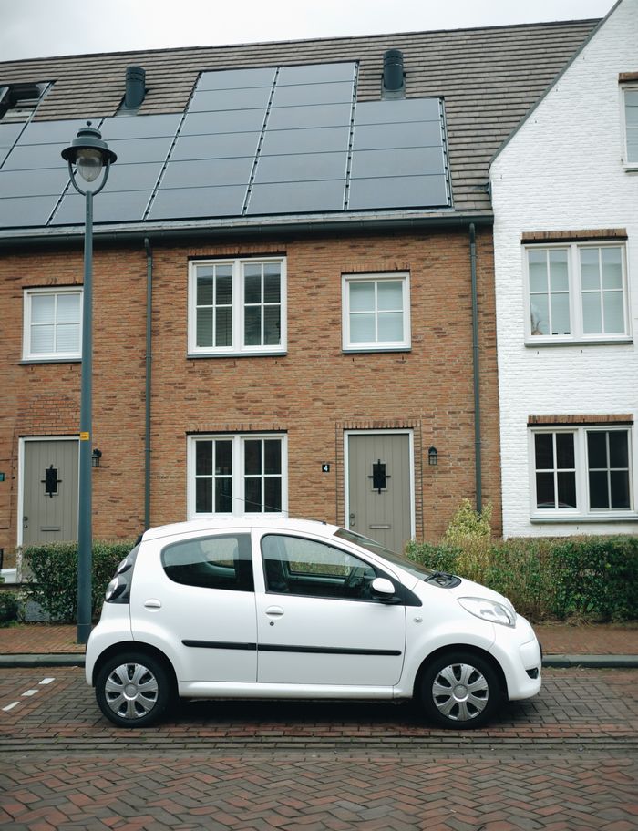 gallery-03 A white car parked in front of modern townhouses with solar panels in Hoofddorp, Netherlands.